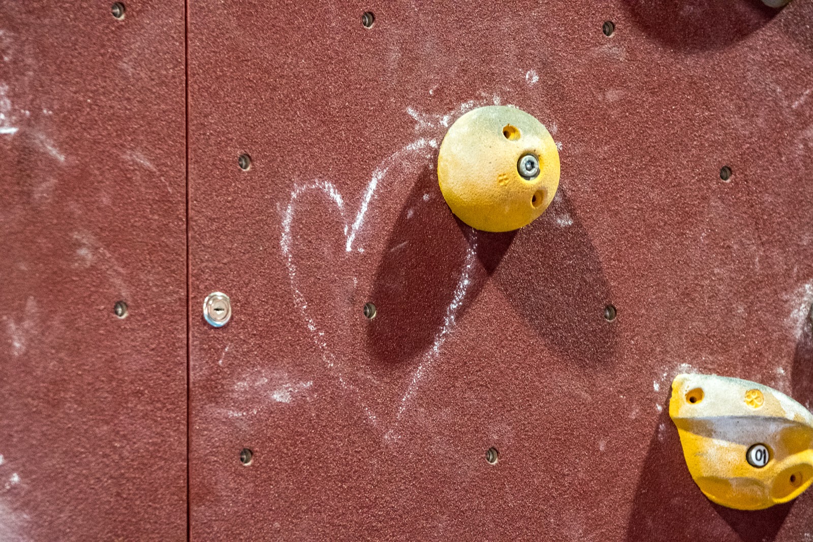 Wand mit darauf befestigten zwei gelben Tritten zum Bouldern. Neben dem einen Tritt ist mit Kreide ein Herz aufgemalt.