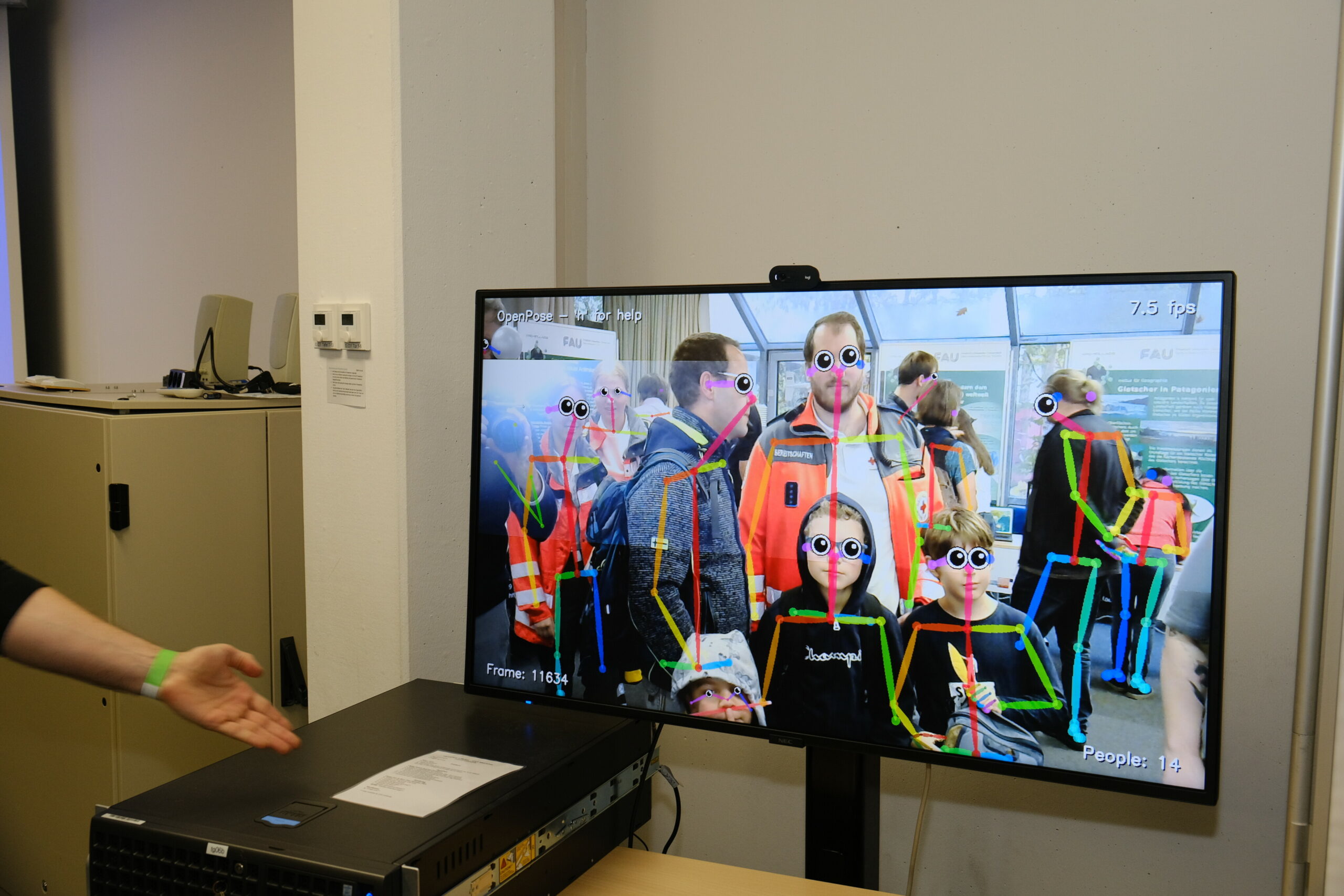 Zu sehen ist ein Bildschirm mit Menschen darauf bzw. deren Körperbewegungen mit bunten Strichen auf dem Bild.