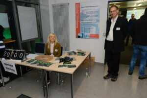 Im Foyer des RRZE stehen zwei Tische an denen eine blonde Frau sitzt. Daneben steht ein Mann mit kurzen Haaren und schwarzem Anzug.