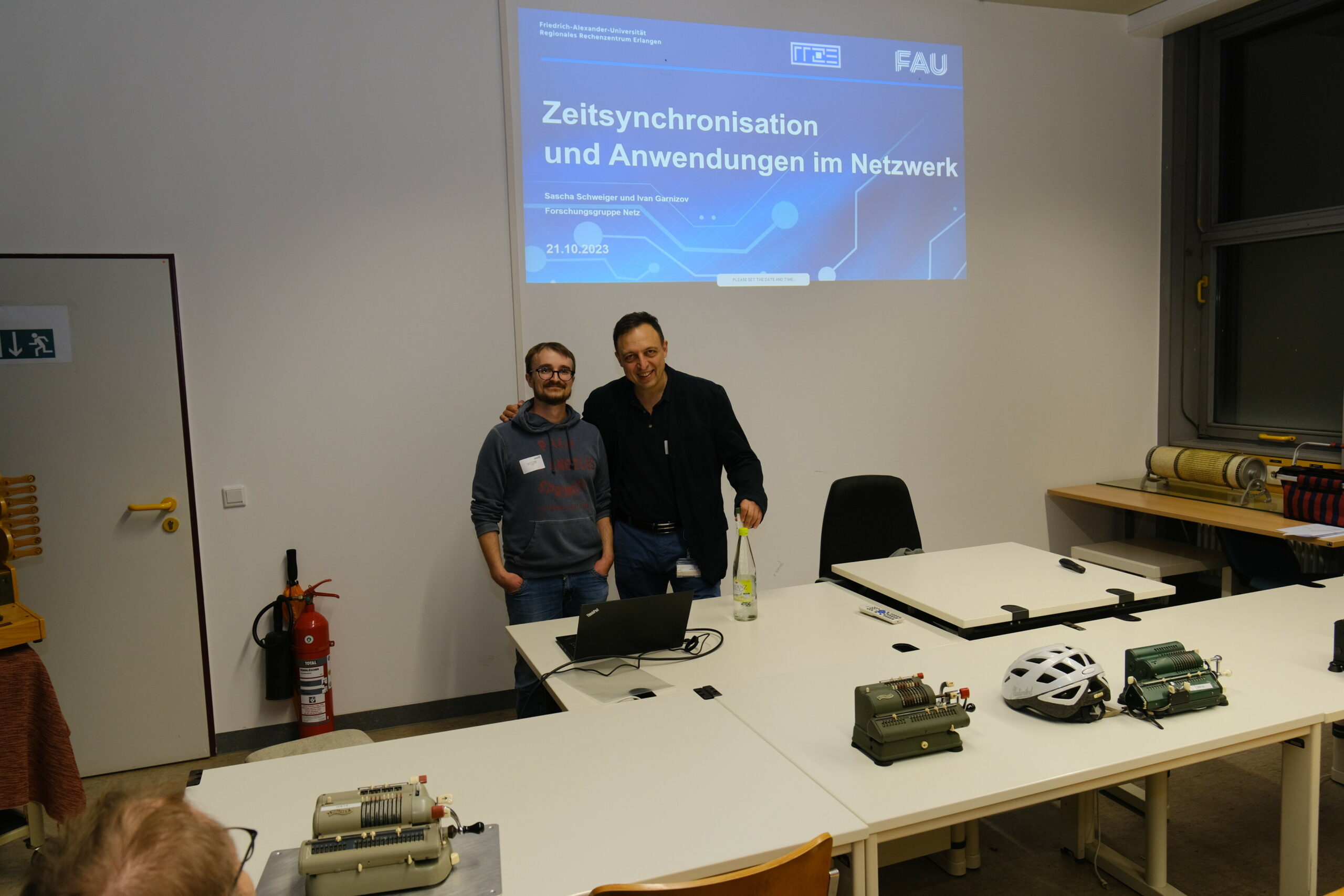 Sascha Schweiger und Ivan Garnziov stehen vor der Titelfolie ihrer Präsentation zur Langen Nacht der Wissenschaften. Beide tragen schwarze Kleidung.